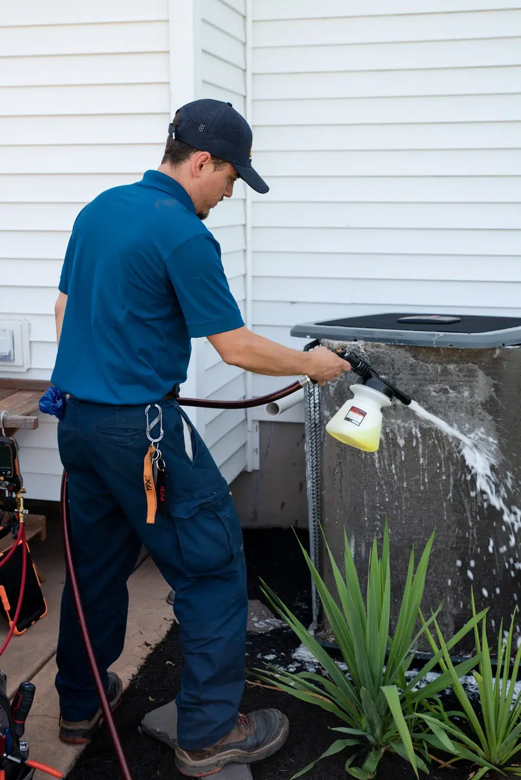 Emerald technician spraying coil cleaner onto an outdoor air conditioner during maintenance