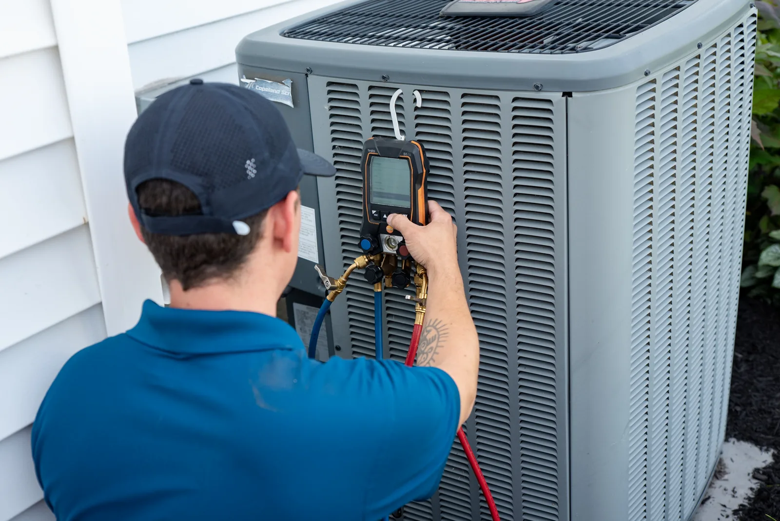 Emerald technician checking refrigerant pressure on an outdoor AC condenser at a Western NY home