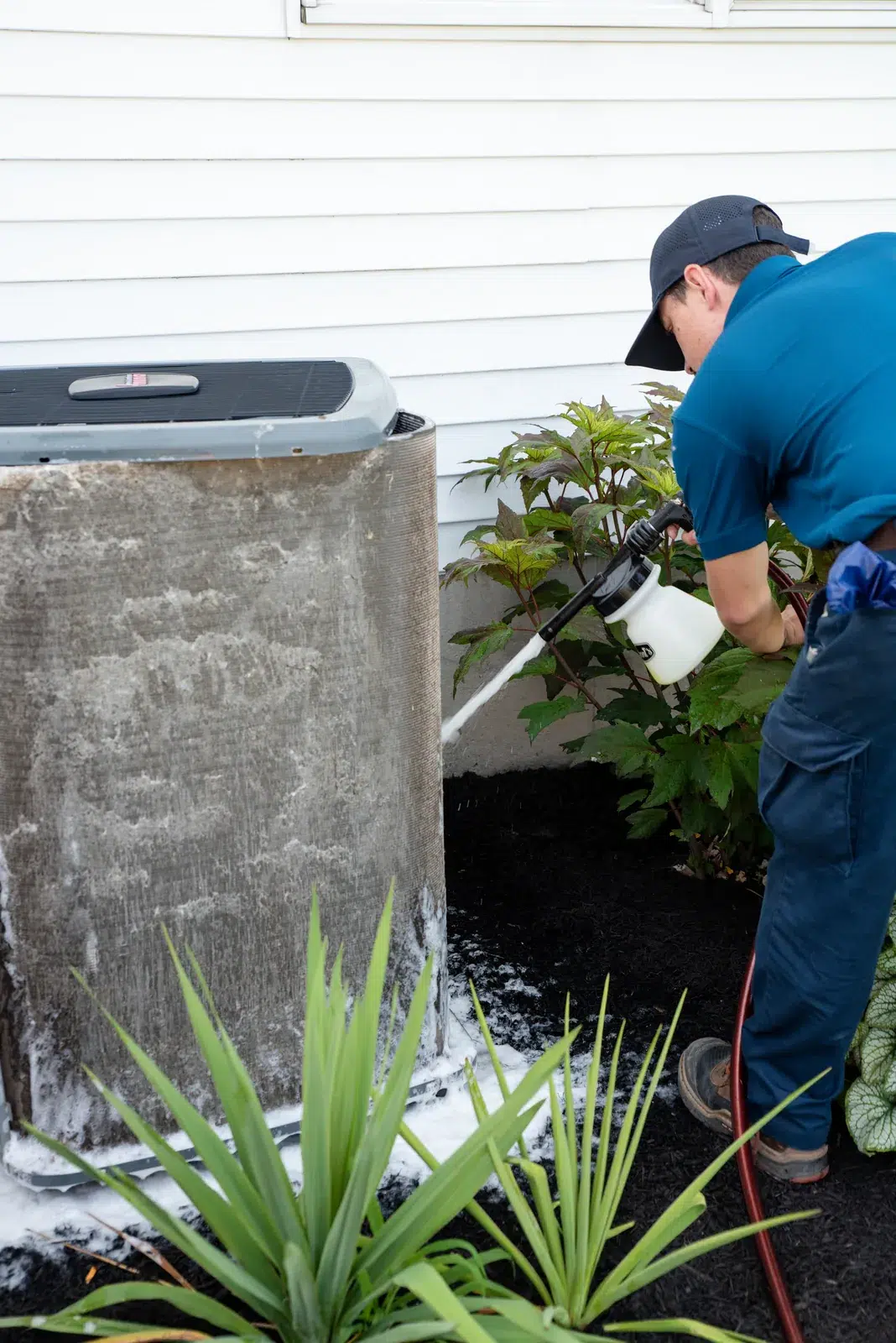 Emerald technician cleaning an outdoor air conditioning unit during a summer service call