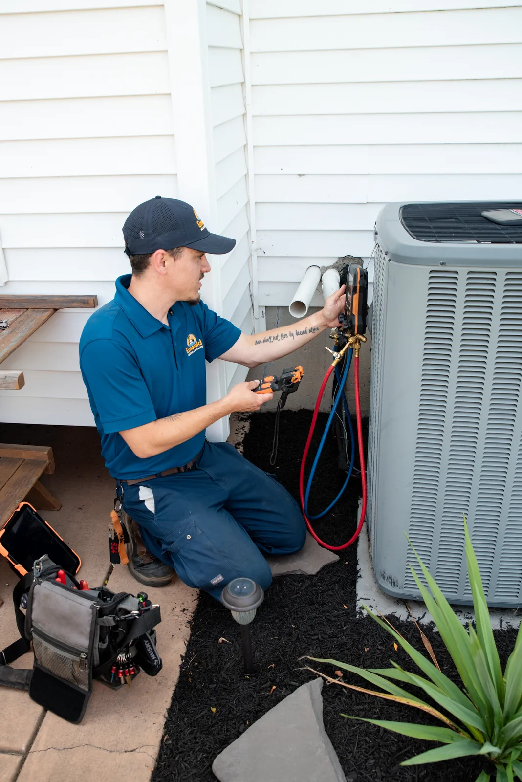 Emerald technician connecting gauges to an outdoor AC condenser beside a Western NY home