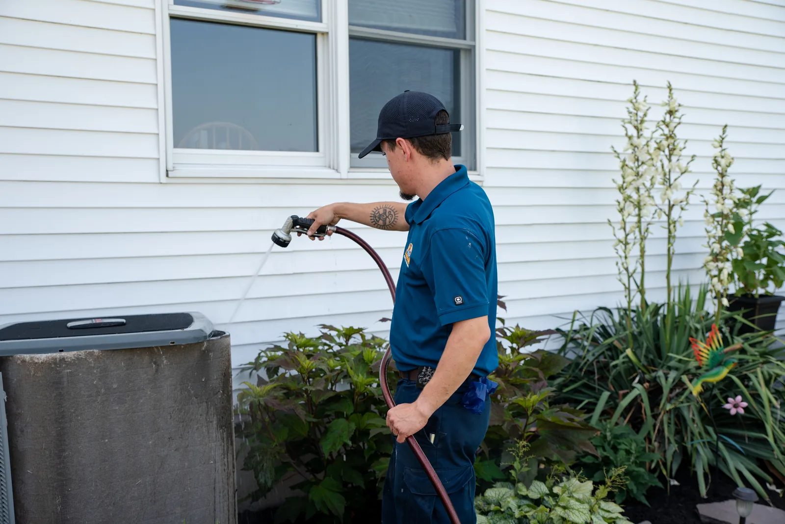 Emerald technician rinsing an outdoor air conditioner condenser during a maintenance visit