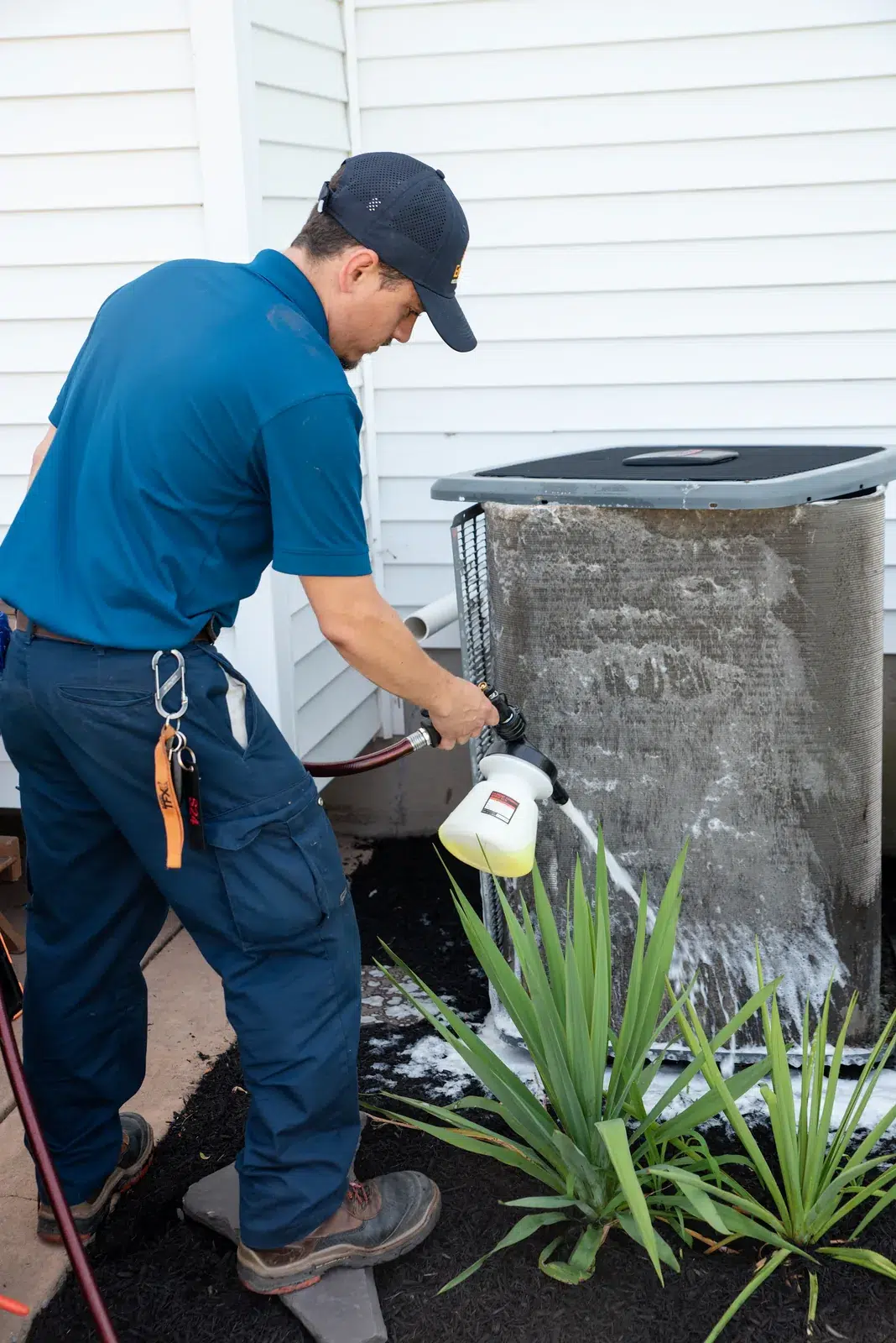 Emerald technician rinsing cleaner from an outdoor condenser coil at a Buffalo area home