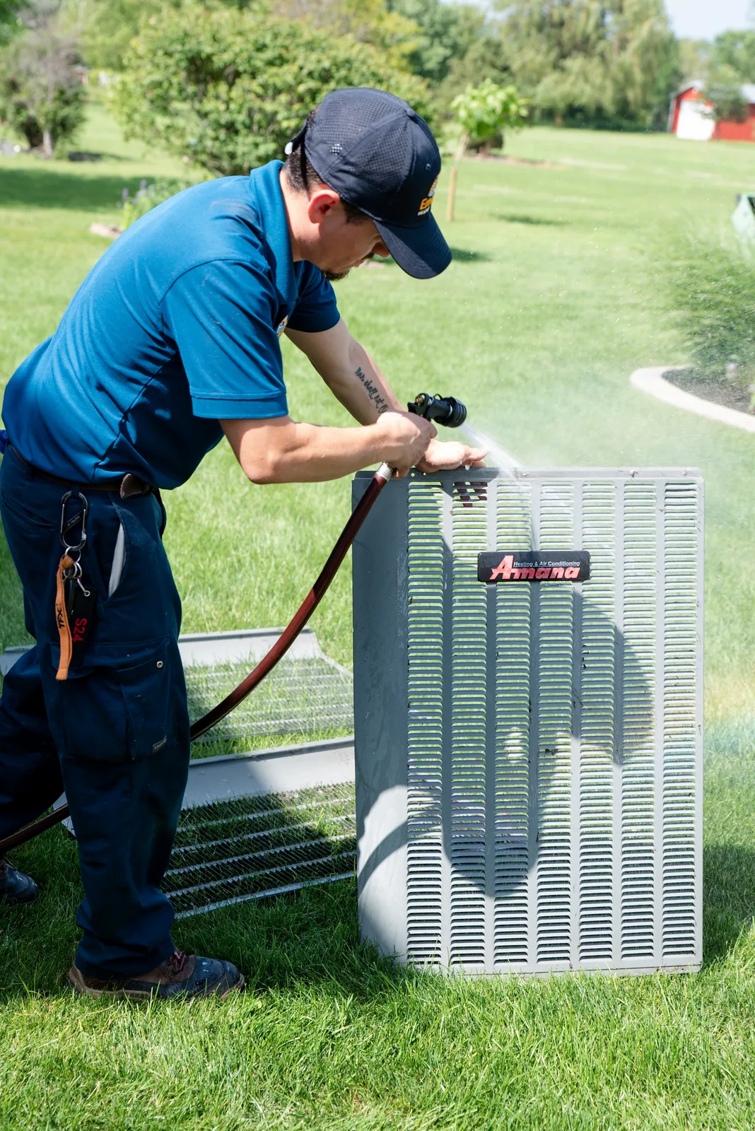 Emerald technician rinsing a condenser coil outdoors during air conditioning maintenance